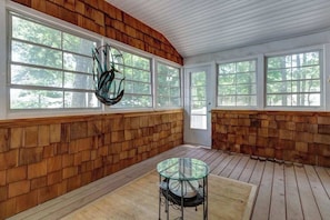 Eine überdachte Veranda mit Holzwänden, großen Fenstern und einem Glastisch.