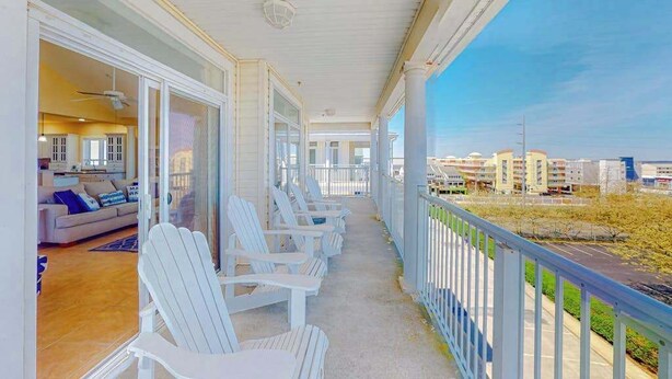 A covered balcony with white Adirondack chairs, a view of the cityscape, and a glimpse of the interior with a sofa and a ceiling fan. - Key Largo Penthouse w/ Ocean View, W/D, WiFi, AC - Half a Block to the Beach (Ocean City)