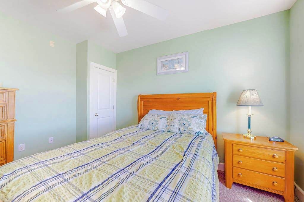 A bedroom with a bed, a nightstand, a lamp, a door, and a ceiling fan.