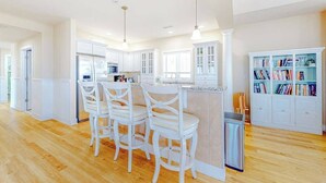 A spacious kitchen with white cabinetry, a central island with bar stools, pendant lighting, and a bookshelf filled with books. - Key Largo Penthouse w/ Ocean View, W/D, WiFi, AC - Half a Block to the Beach (Ocean City)