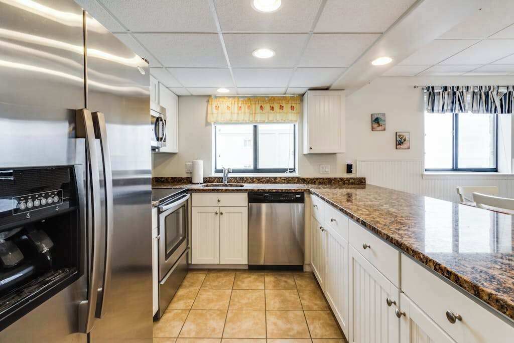 A modern kitchen with stainless steel appliances, white cabinetry, a granite countertop, and a window with a view.
