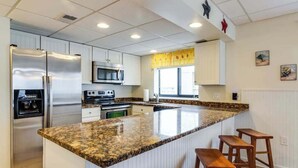 Cucina con piano di lavoro in granito, elettrodomestici in acciaio inossidabile e sgabelli da bar in legno.