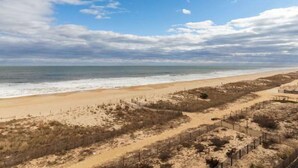 Una spiaggia con un sentiero sabbioso, una recinzione e una vista libera sull'oceano.