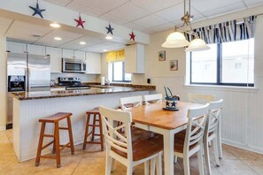 Une cuisine avec des meubles blancs, un îlot central et un coin repas avec des chaises blanches.