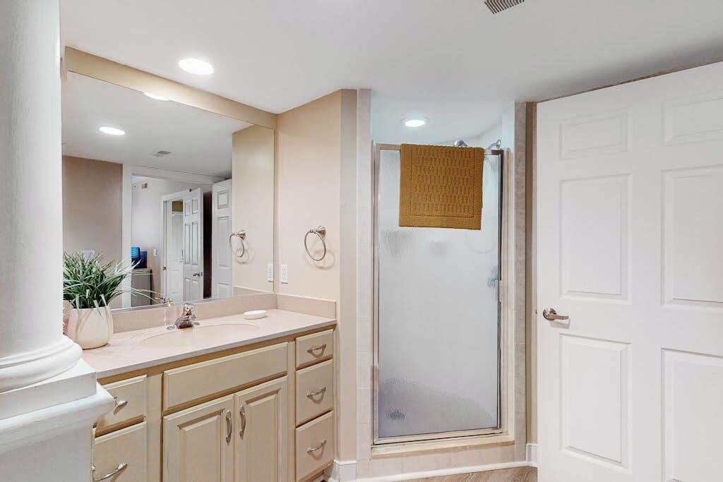 A bathroom with a large mirror, a sink, a shower with a glass door, and a towel hanging on the door.