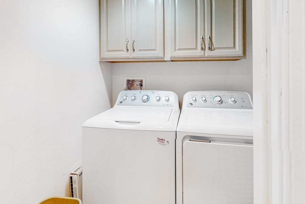 A laundry room with two white washing machines and a cabinet above them.