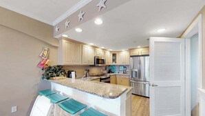 A kitchen with a central island, bar stools, a refrigerator, and a microwave. - Adagio 407 (Ocean City)