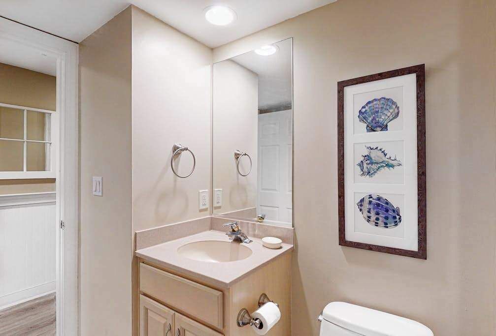 A bathroom with a sink, mirror, toilet, and framed artwork on the wall.