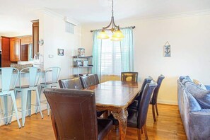 A dining area with a wooden table and chairs, a kitchen in the background, and a blue sofa.