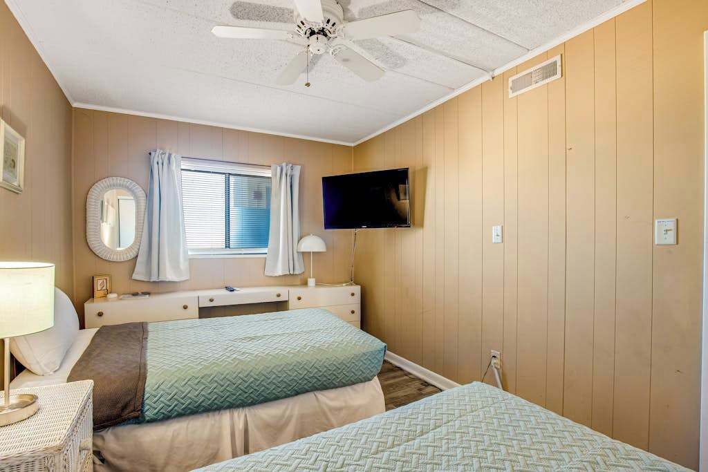 A bedroom with two beds, a ceiling fan, a TV, a window with curtains, and a bedside table.