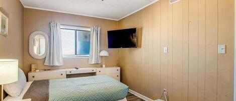 A bedroom with two beds, a ceiling fan, a TV, a window with curtains, and a bedside table.