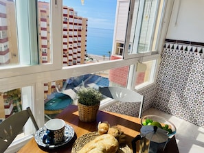 A balcony with a view of the sea, a table with a cup, bread, a plant, and a fruit bowl. - Apartamento Faro 77 by At Home Costa del Sol (Torrox)