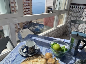 A balcony with a table set with a cup, a bowl of fruit, and pastries, overlooking a coastal view. - Apartamento Faro 77 by At Home Costa del Sol (Torrox)