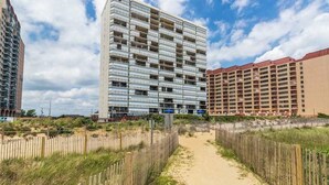 A multi-story hotel with a central courtyard, surrounded by a sandy path and wooden fences. - Irene 1106 (Ocean City)