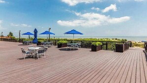 A wooden deck with outdoor tables and chairs, blue umbrellas, and a view of the sea. - Irene 1106 (Ocean City)