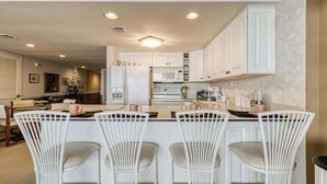 A kitchen with white cabinetry, a central island with bar stools, and recessed ceiling lighting. - Irene 1106 (Ocean City)