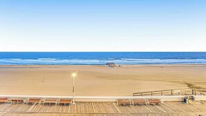 A beach view from a wooden deck with lounge chairs and a railing. - Decatur House 203 (Ocean City)