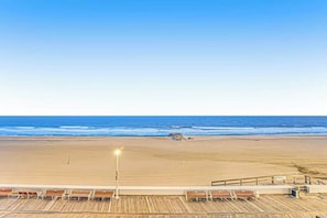 A beach view from a wooden deck with lounge chairs and a railing. - Decatur House 203 (Ocean City)