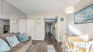 A modern living room with a sofa, coffee table, and dining area with chairs. - Decatur House 203 (Ocean City)