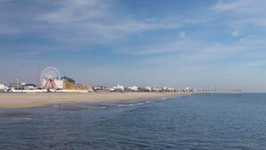 Ein Strand mit einem Steg, der ins Wasser führt, einem Riesenrad und Gebäuden entlang der Küste.