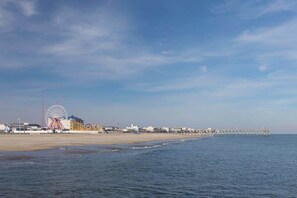 Ein Strand mit einem Steg, der ins Wasser führt, einem Riesenrad und Gebäuden entlang der Küste.