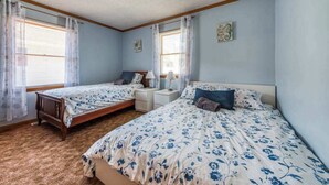 Ein Schlafzimmer mit zwei Betten, einem Fenster mit Vorhängen, einem Nachttisch und einer Wanduhr.