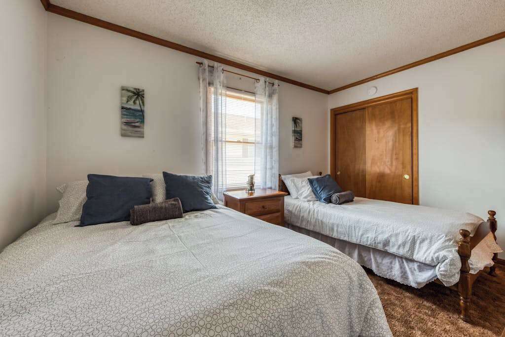 A bedroom with two beds, a wooden wardrobe, a nightstand, and a window with curtains.