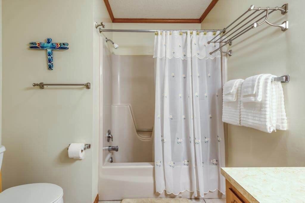 A bathroom with a shower curtain, a towel rack, a toilet, and a wall-mounted towel rack.