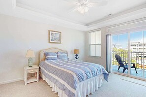 Ein Schlafzimmer mit Bett, Nachttisch, Lampe, einem Bild an der Wand und Blick durch ein großes Fenster hinaus.