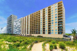 A high-rise hotel with multiple balconies, a sandy pathway, and a clear blue sky. - Oceanfront, Renovated Marigot Beach Condo w/ Ocean View, AC, W/D (Ocean City)