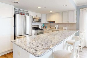 A modern kitchen with white cabinets, stainless steel appliances, and a marble countertop. - Oceanfront, Renovated Marigot Beach Condo w/ Ocean View, AC, W/D (Ocean City)