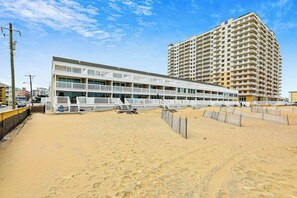 Un hôtel situé en bord de mer, avec une structure à plusieurs étages, une plage de sable devant et un grand bâtiment en arrière-plan.