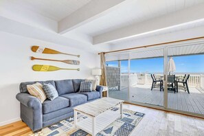 Una stanza con un divano grigio, un tavolino in legno e vista sul mare tramite un'ampia porta scorrevole in vetro.