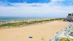 Een strand met een hek, strandparasols en een gebouw met een plat dak.