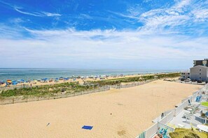 Une plage avec une clôture, des parasols et un bâtiment doté d’un toit plat.