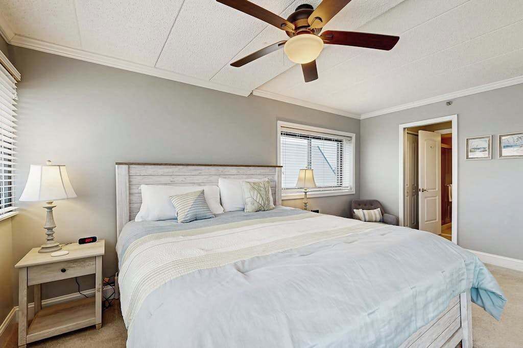 Un dormitorio con cama, mesitas de noche, ventilador de techo y ventana.