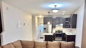 A living room with a sectional sofa, a round coffee table, and a kitchen in the background. - Spacious 3BR Family Home | 2 King Beds & queen bed,Big Deck & Garage & free wifi (Winnipeg)
