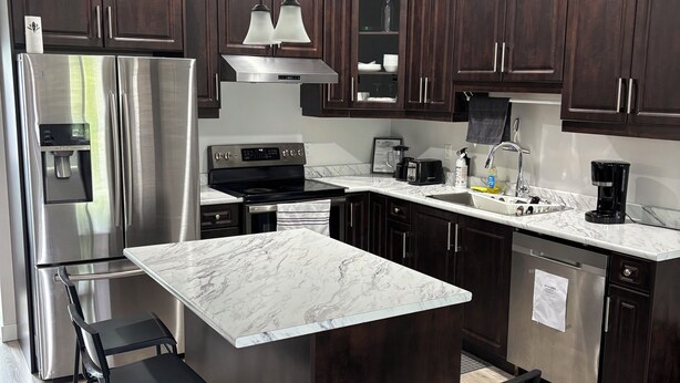 A modern kitchen with dark wood cabinets, stainless steel appliances, a marble island, and black bar stools. - Spacious 3BR Family Home | 2 King Beds & queen bed,Big Deck & Garage & free wifi (Winnipeg)