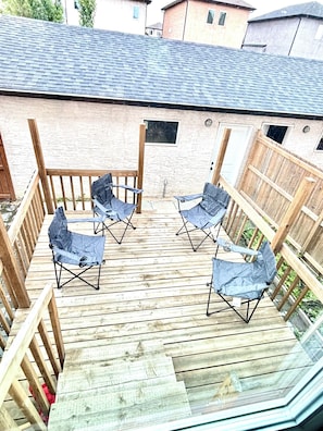 A deck with four blue folding chairs, a wooden railing, and a view of a house with a sloped roof.