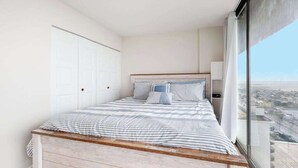 Une chambre à coucher comprenant un lit, une table de chevet, une fenêtre donnant sur la ville et un placard.