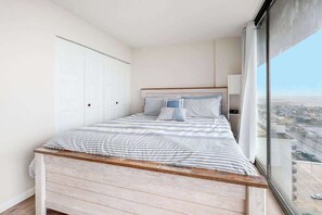 A bedroom with a bed, a nightstand, a window with a city view, and a closet. - Oceanfront Getaway w/ Private Balcony, Free WiFi, Beach Access & Shared Pool (Ocean City)