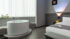 A modern hotel room with a large bathtub, a neatly made bed, and a bedside table with a lamp. - Banana FUN Hotel (Guangzhou Beijing Road Pedestrian Street Yuexiu Park) (Guangzhou)