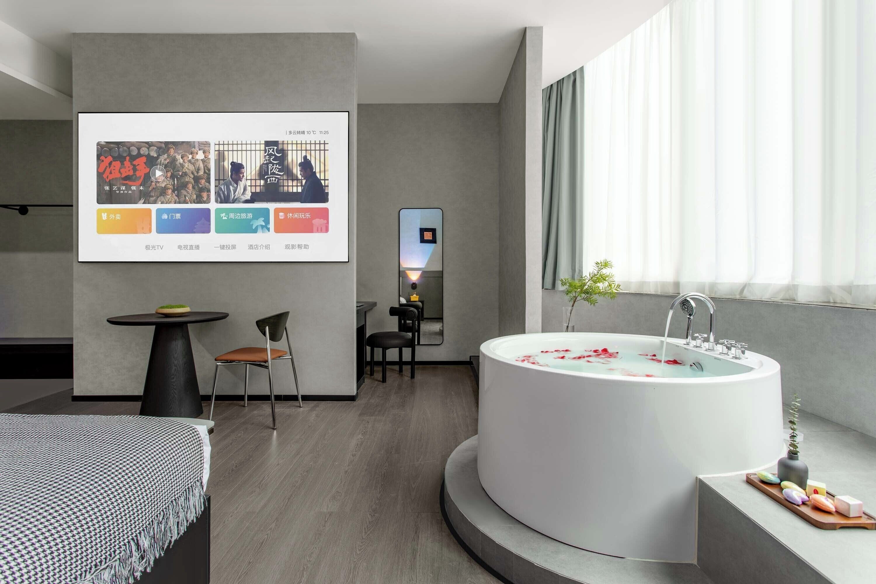 A modern bathroom with a freestanding bathtub, a small table with chairs, and a large window with curtains.