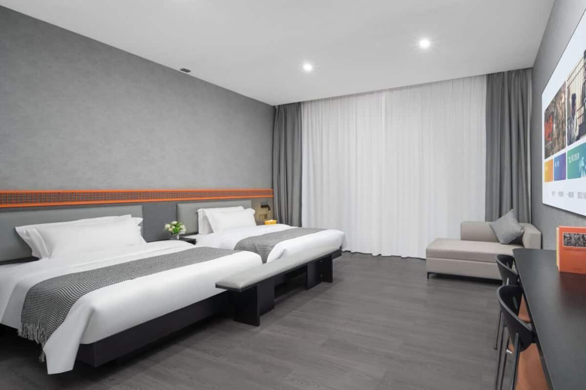 Habitación de hotel con dos camas, un sofá, un escritorio y un ventanal con cortinas.