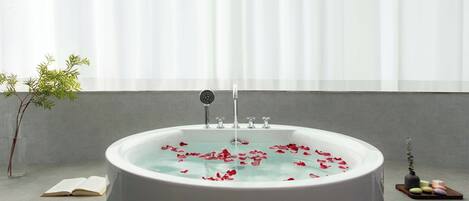 Une baignoire remplie de pétales de rose, un livre et une petite plante posée sur le rebord d’une fenêtre.