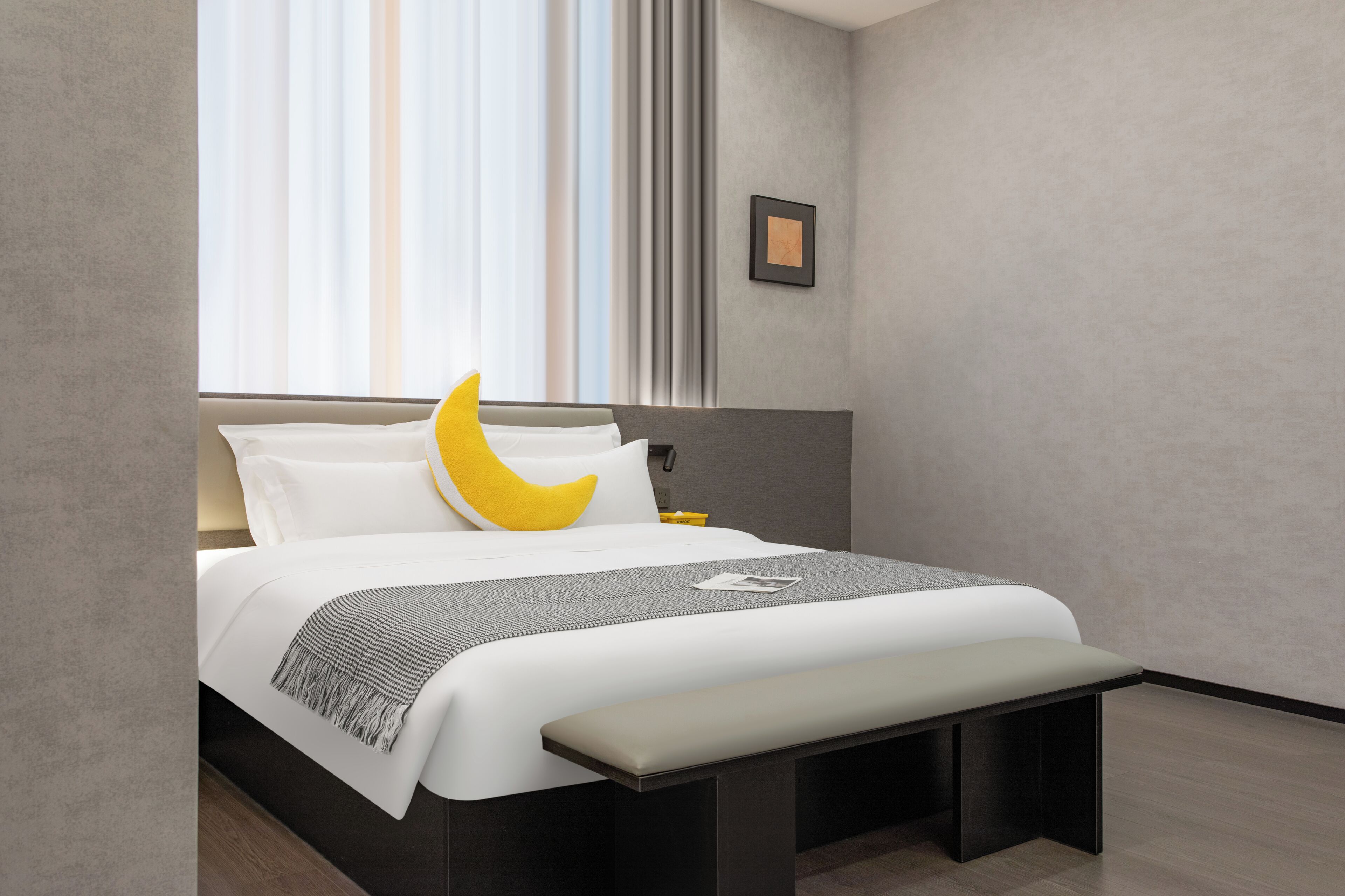 Et moderne hotelværelse med seng, sengebord, bænk og et billede i ramme på væggen.