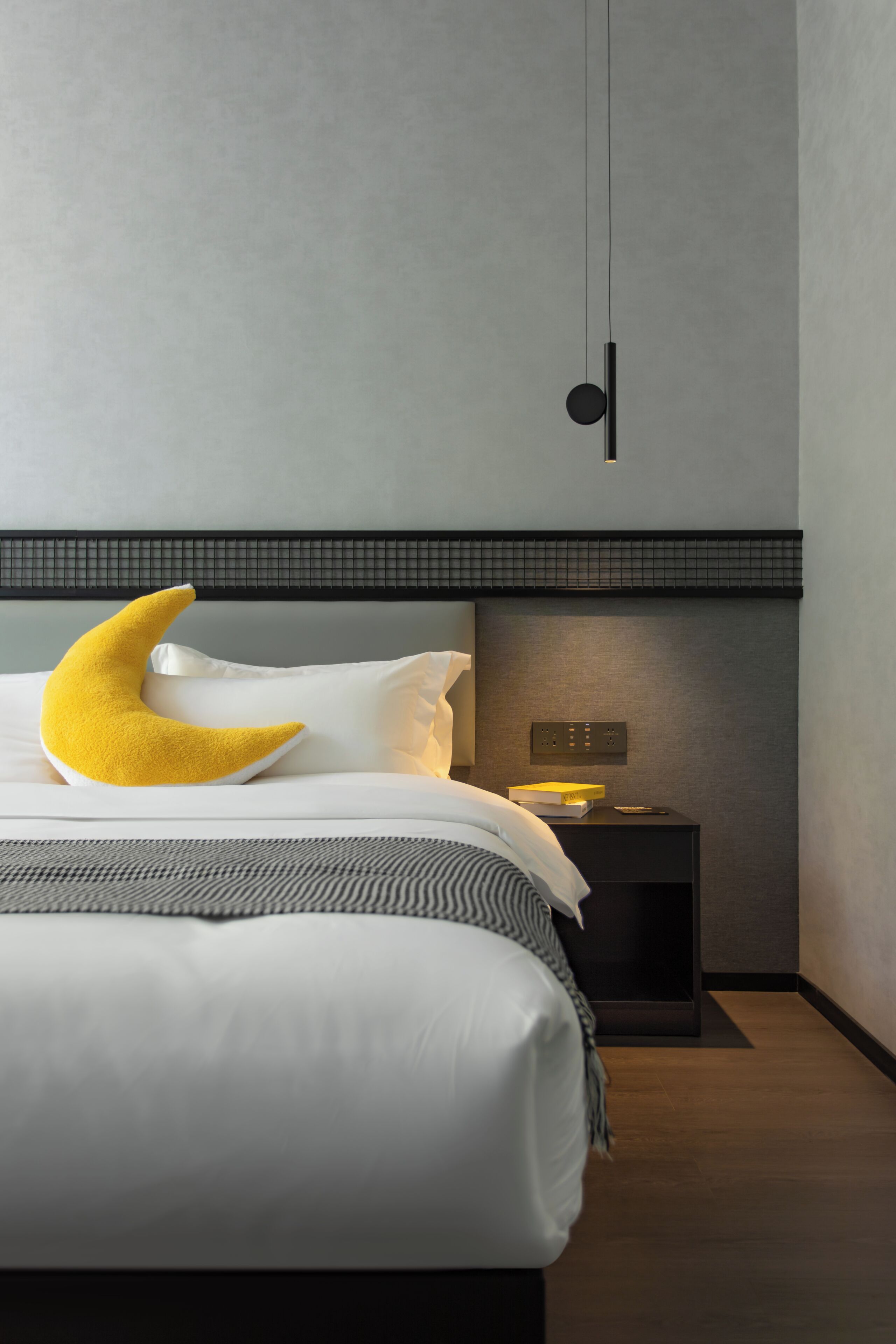 Una camera da letto moderna con un letto, un comodino, una lampada a parete e un cuscino a forma di mezzaluna.