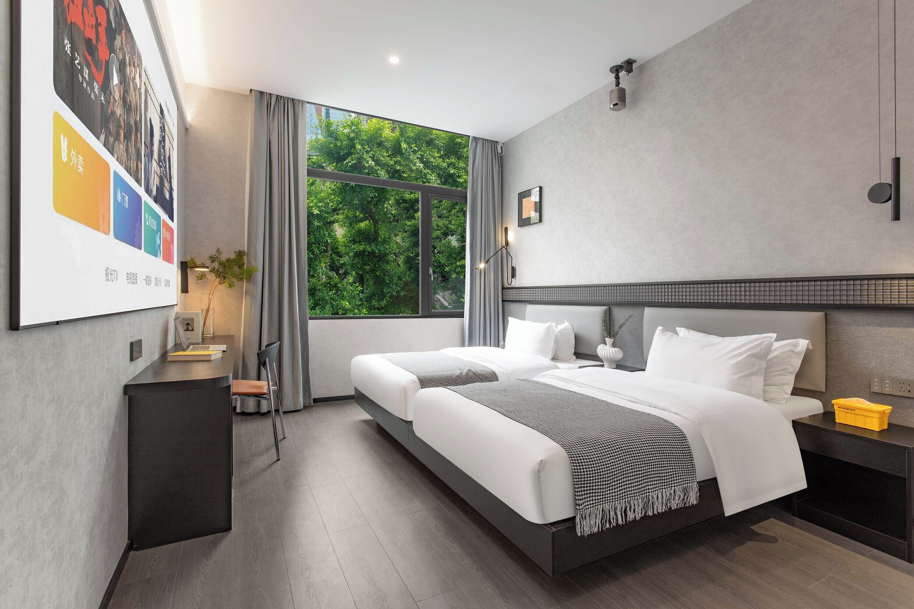 Ett modernt hotellrum med två sängar, ett stort fönster, ett skrivbord och utsikt över grönområden utanför.