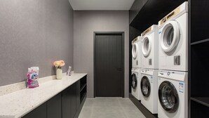 A laundry room with a washing machine and dryer, a door, and a countertop with a bag of detergent and a vase. - Banana FUN Hotel (Guangzhou Beijing Road Pedestrian Street Yuexiu Park) (Guangzhou)