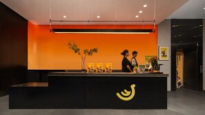 A reception desk with a black counter, a yellow logo, and two individuals standing behind it. - Banana FUN Hotel (Guangzhou Beijing Road Pedestrian Street Yuexiu Park) (Guangzhou)